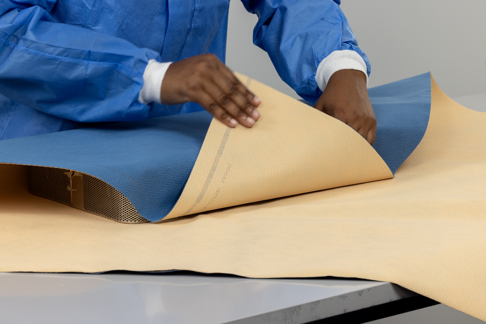 Operatiekamerarts tilt een vel ARMOR-FLEX sterilisatiewrap, waarop het SteelBlue buitengezicht en het amber ASSURE-DRY binnengezicht te zien zijn