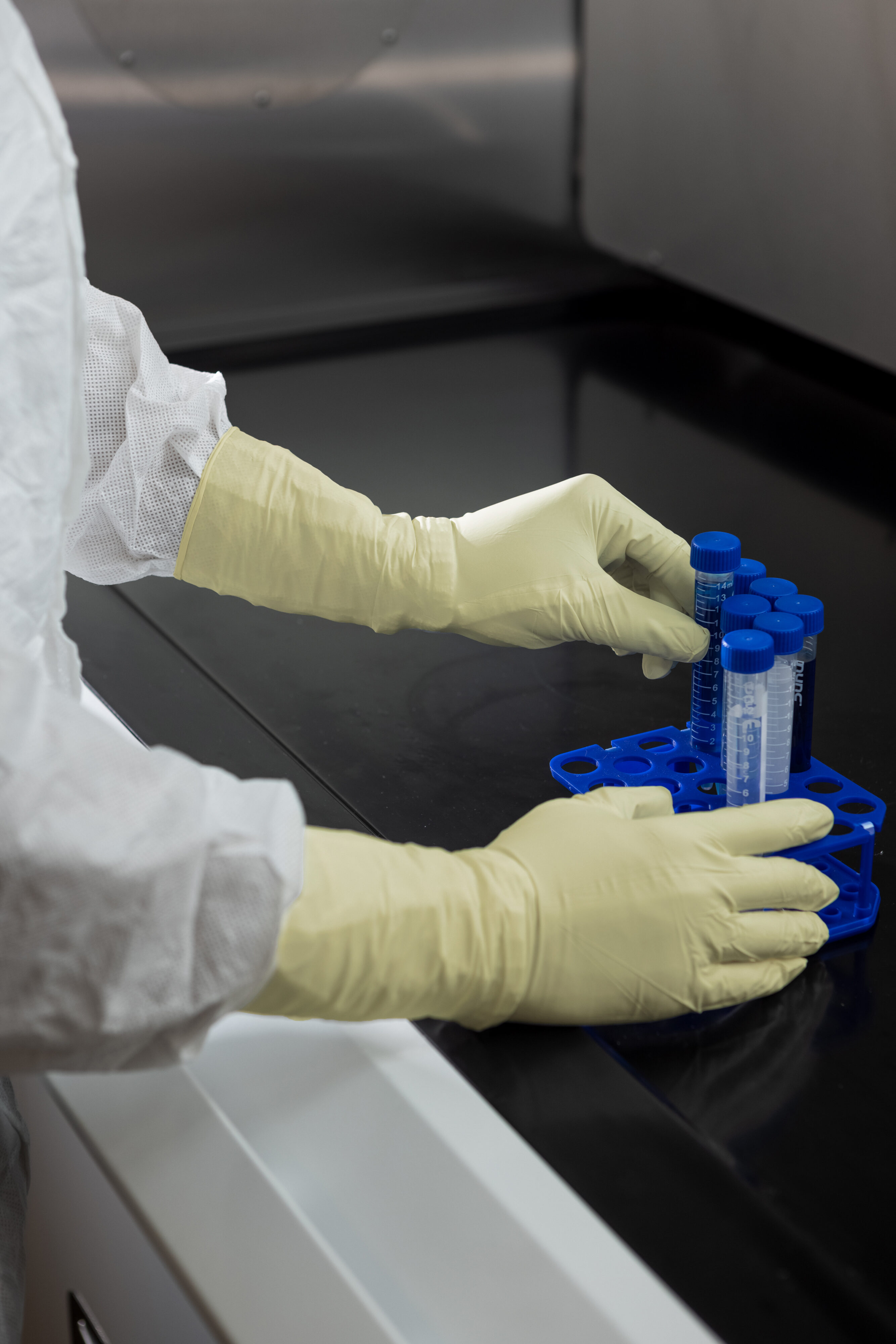 Gloved hands placing sample tubes into a rack during hazardous drug handling