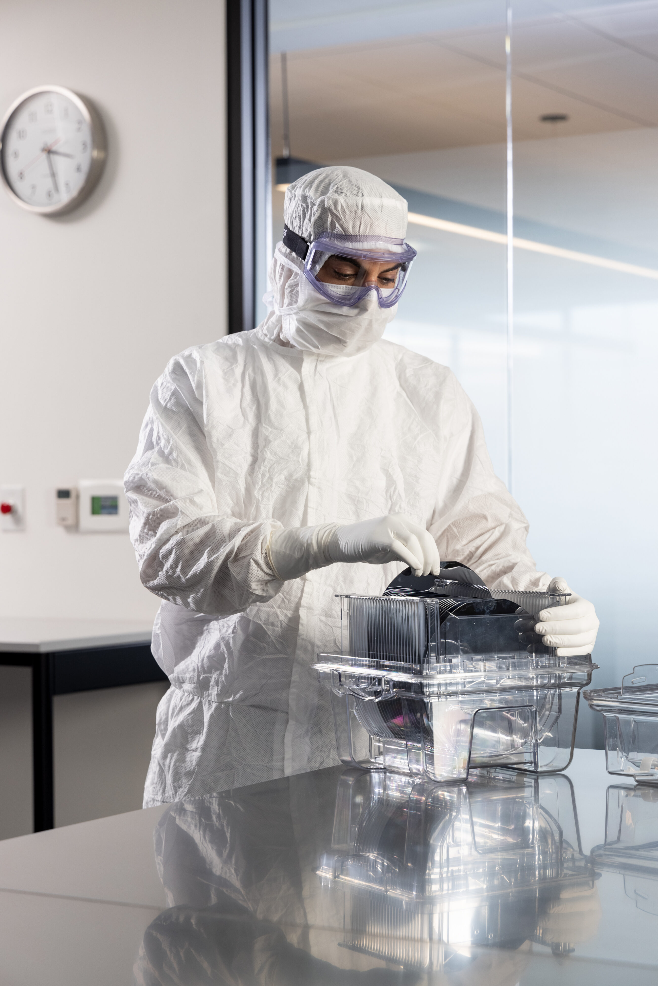 Cleanroom technician in coveralls and PUREZERO gloves handling a wafer carrier